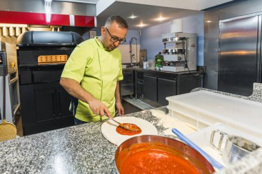 Şef pizza hamuruna taze domates sosu ekliyor. Pizza malzemeleri. Yüksek kalite fotoğraf