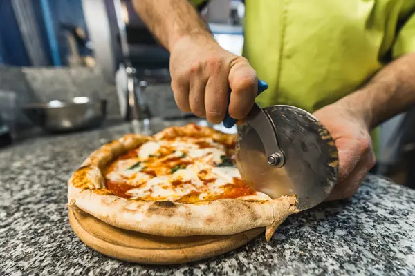 Aşçı pizza margherita 'yı pizza bıçağıyla kesiyor. Mutfaktaki tahta tahtada. Yüksek kalite fotoğraf