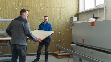 İşçiler fabrika makinesine ahşap bir tahta getiriyorlar, ahşap ürünler üretiyorlar. Yüksek kalite fotoğraf