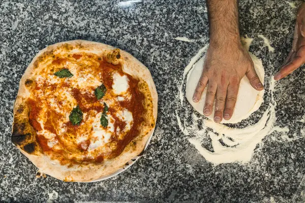 Odgórne Ujęcie Rąk Przygotowujących Ciasto Pizzowe Obok Przygotowanej Pizzy Margherita Zdjęcie Stockowe