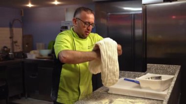 Üniformalı profesyonel bir şef restoran mutfağında kocaman bir pizza hamuru tutuyor. Yüksek kalite 4k görüntü