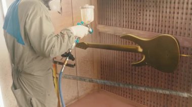 Elektro gitarın vücudunu bronz renge boyayan bir adam. Yüksek kalite 4k görüntü