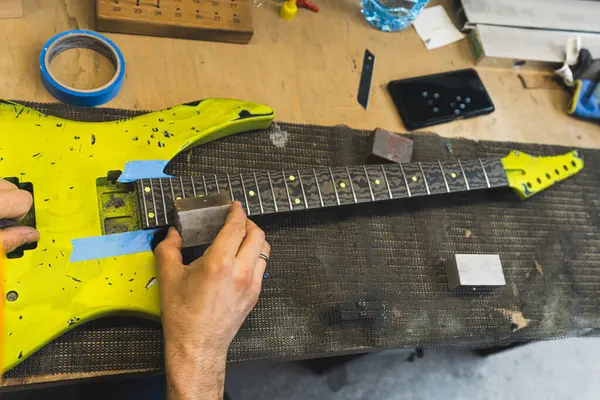 stock image worker repairing a yellow electric guitar on his working table, music concept, how to smooth sharp fret ends on the guitar. High quality photo