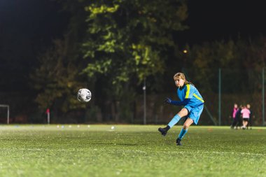 Küçük bir kızın antrenmanda futbol topunu tekmelerken çekilen fotoğrafı, dışarıda, gece geç saatlerde. Yüksek kalite fotoğraf