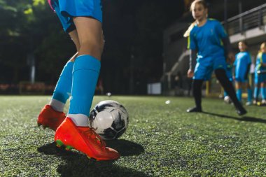 Stadyumda futbol topuyla oynayan bir kızın yakın plan fotoğrafı, akşam antrenmanı, mavi üniformalar. Yüksek kalite fotoğraf