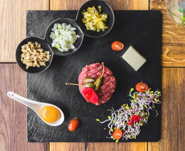 Gurme tartar ve aksesuarların canlı bir düzenini deneyimleyin, sanatsal olarak karanlık bir tabakta sunuluyor, aşçılık sanatını sergiliyor ve yemek meraklıları için mükemmel lezzetler sunuyor..