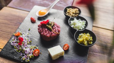 Gurme tartar ve aksesuarların canlı bir düzenini deneyimleyin, sanatsal olarak karanlık bir tabakta sunuluyor, aşçılık sanatını sergiliyor ve yemek meraklıları için mükemmel lezzetler sunuyor..