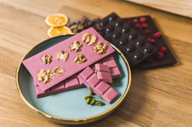 Fındık, kurutulmuş meyve ve şam fıstığı ile süslenmiş pembe ve koyu renkli çikolatalar, ahşap bir masada zarif bir şekilde servis edilir..