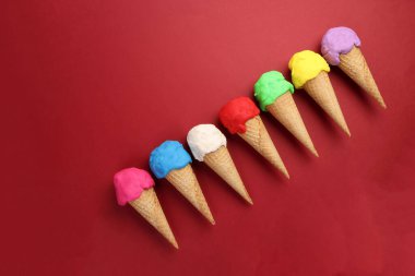 Sahte modelleme kil renkli dondurma kepçesi waffle bisküvi konisi düz kırmızı zemin üzerinde yatıyordu 