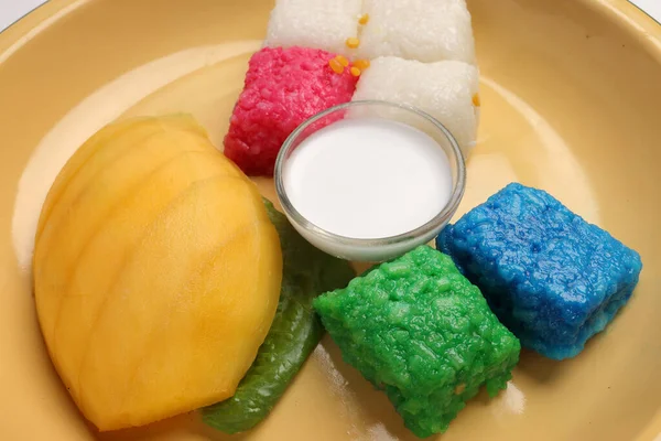 Thai sweet desert red blue yellow white mango sticky rice with coconut cream milk on enamel tin metal plate wood spoon