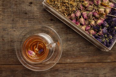 Kuru çiçek çayı kelebek bezelye çiçeği şeffaf cam çay fincanı kırsal ahşap masa arka planında 