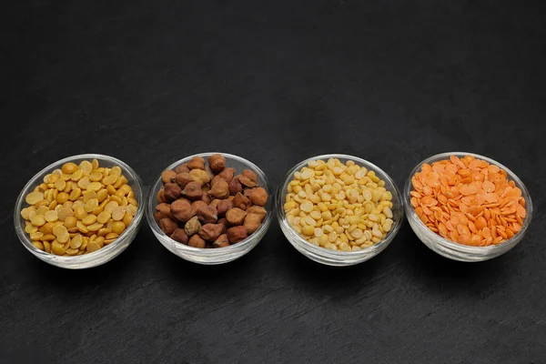 variety of lentils pulses red masoor mung dal yellow split chickpeas pigeon peas in mini glass bowl on black slate background