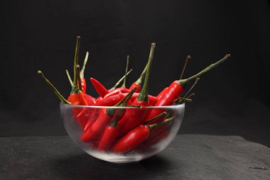 Kırmızı sıcak kuşların gözü siyah arka planda cam kasede kırmızı biber. 