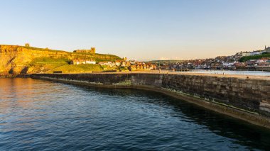 Whitby, Kuzey Yorkshire, İngiltere - 21 Haziran 2023 Doğu Kayalıkları ve St. Mary Kilisesi 'ndeki evler üzerinde altın saat