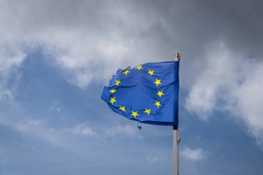 A torn EU flag blows in the wind with a few clouds in the background, seen in Pevensey Bay, East Sussex, England, UK clipart