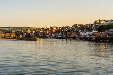 Whitby, North Yorkshire, İngiltere - 21 Haziran 2023 Batı Kayalıkları 'ndaki ve Pier Rd' deki evlerin üzerinde altın saat