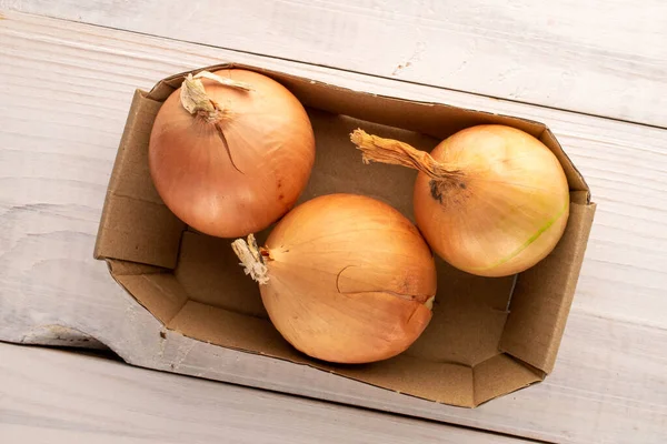 Three ripe organic onions in a paper dish on a wooden table, close-up, top view.