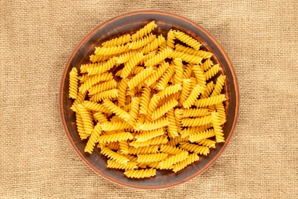 Durum wheat pasta in a clay plate on a jute cloth, macro, top view.