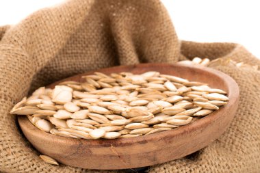 Ahşap bir tabakta soyulmamış çiğ balkabağı tohumları, jüt çantalı, makro, beyaz arka planda izole edilmiş..