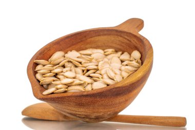 Ahşap bir fincanda soyulmamış çiğ balkabağı tohumları, tahta bir kaşık, makro, beyaz arka planda izole edilmiş..