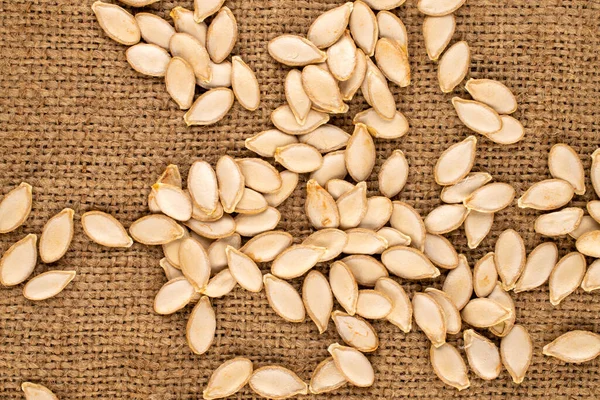 stock image Unpeeled raw pumpkin seeds  on jute cloth, macro, top view.