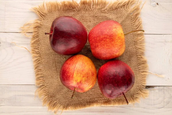 Several red juicy apples with jute napkin on wooden table, macro, top view.