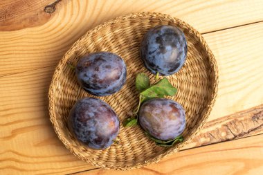 Birkaç organik siyah erik bir saman tabağında, yakın planda, ahşap bir masada, üst tarafta..
