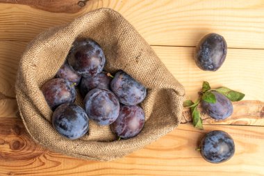 Birkaç sulu siyah erik jüt torbasında, yakın planda, ahşap bir masanın üstünde, üst tarafta..