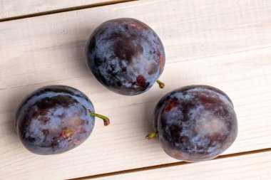 Üç organik siyah erik, yakın plan, beyaz ahşap bir masanın üstünde, üst manzara..