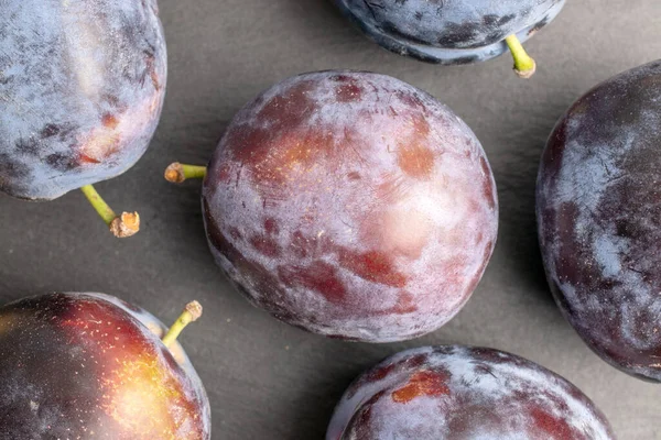 stock image Several organic black plums, close-up, on a slate board, top view.