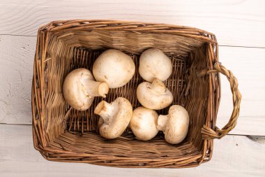 Birkaç organik taze iştah açıcı mantar şampiyonu hasır sepetli, yakın plan, doğal ahşap bir masa üzerinde, beyaza boyanmış, üstten manzara..