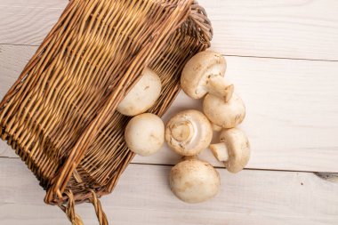 Birkaç organik taze iştah açıcı mantar şampiyonu hasır sepetli, yakın plan, doğal ahşap bir masa üzerinde, beyaza boyanmış, üstten manzara..
