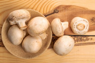 Birkaç organik taze iştah açıcı mantar şampiyonu seramik tabağıyla, ahşaptan yapılmış bir masanın üstünde, üst görünüm.