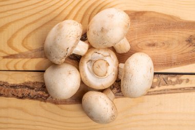 Pek çok organik taze ağız sulandıran şampiyon mantarı, doğal ahşaptan yapılmış bir masanın üstünde, üst görünümde..