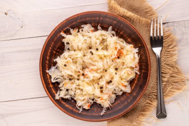 Ahşap bir masa, makro, üst manzara üzerinde kil bir tabakta metal çatallı lahana turşusu..