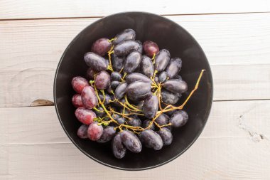 Tahta bir masanın üstünde, siyah seramik bir tabakta, bir demet sulu organik siyah üzüm..