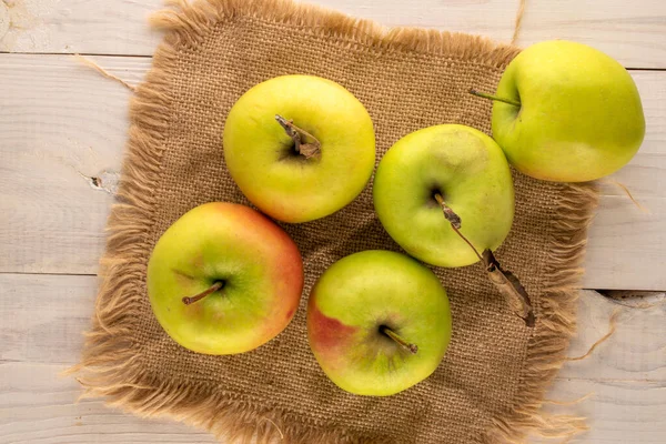 Several sweet green apples with jute napkin on wooden table, macro, top view.