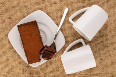 Bir parça mantarlı kek, seramik beyaz çay tabağı ve iki fincan jüt kumaş, makro, üst manzara..