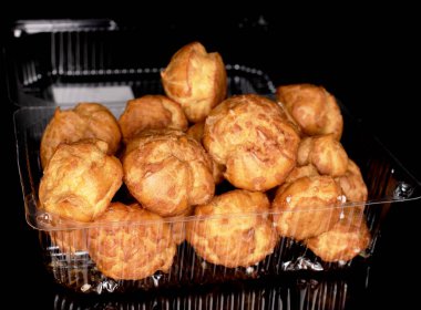 Several delicious chouquettes in a plastic box on a black background.