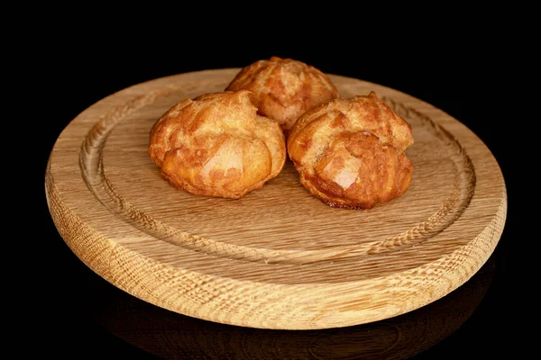 Three fresh chouquettes on a round bamboo tray, on a black background.
