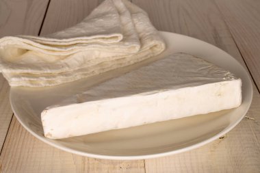 One slice of delicious brie cheese with white ceramic plate on wooden table, macro.