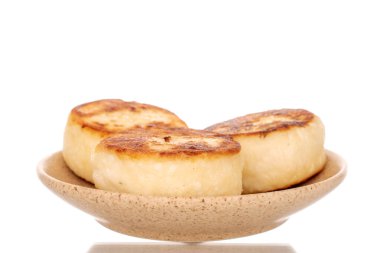 Three homemade cheese pancakes on a ceramic saucer, macro, isolated on a white background.