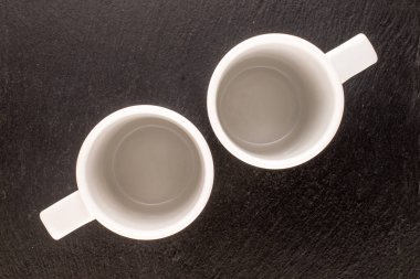 Two empty ceramic white cups on slate stone, macro, top view.