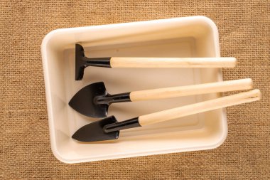 Garden tool with wooden handle in plastic container on jute canvas, macro, top view.