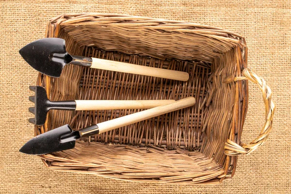 Garden tool with wooden handle in wicker basket on jute canvas, macro, top view.