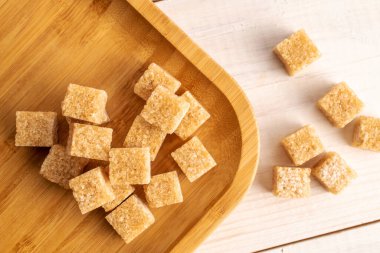Several brown sugar cubes with a bamboo plate, close-up, on a white wooden table.