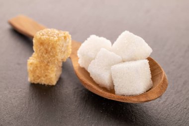 Several cubes of brown and white sugar with a wooden spoon, close-up, on a slate board.