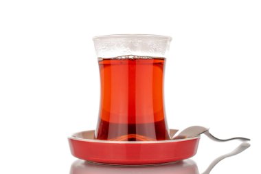 One glass of black aromatic tea with a metal spoon on a ceramic saucer, macro, isolated on white background.