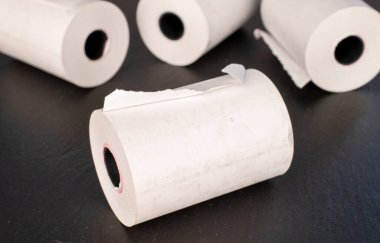 Several paper rolls of cash register tape on slate stone, close-up.