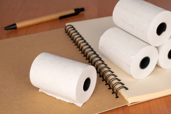 Several paper rolls of cash register tape with notebook and pencil on office desk, close-up.